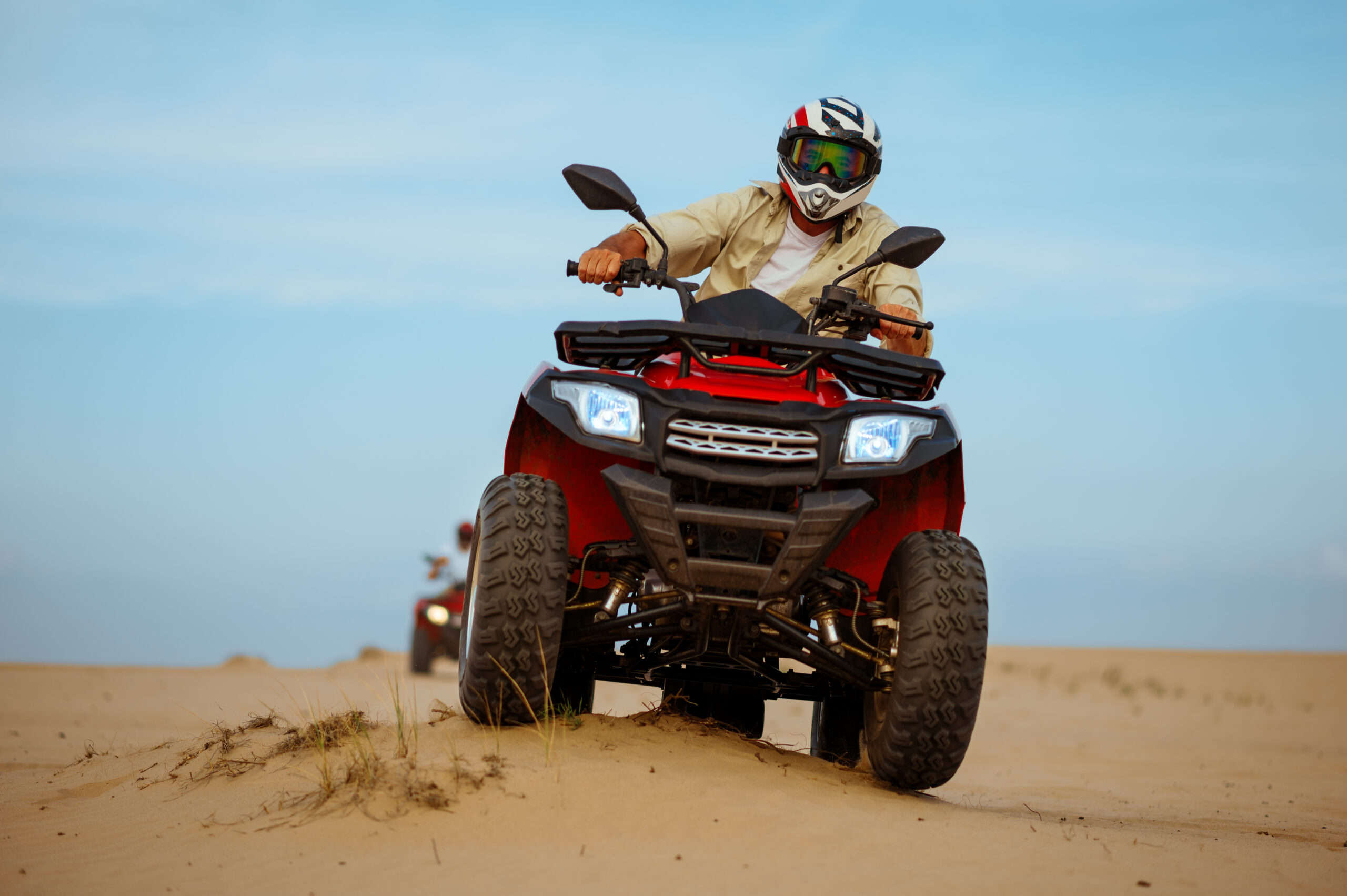 Man in helmet rides on atv, downhill riding in desert sands, action view. Male person on quad bike, sandy race, dune safari in hot sunny day, 4x4 extreme adventure, quad-biking