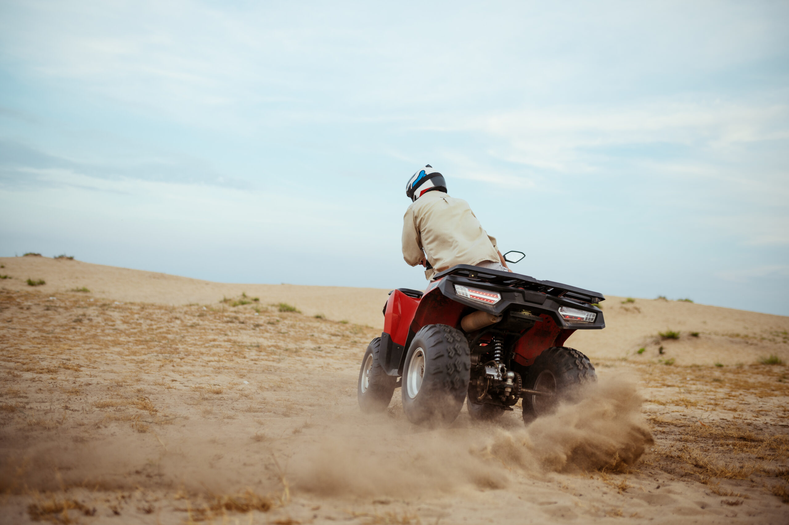 Man in helmet rides on atv, downhill riding in desert sands, action view. Male person on quad bike, sandy race, dune safari in hot sunny day, 4x4 extreme adventure, quad-biking