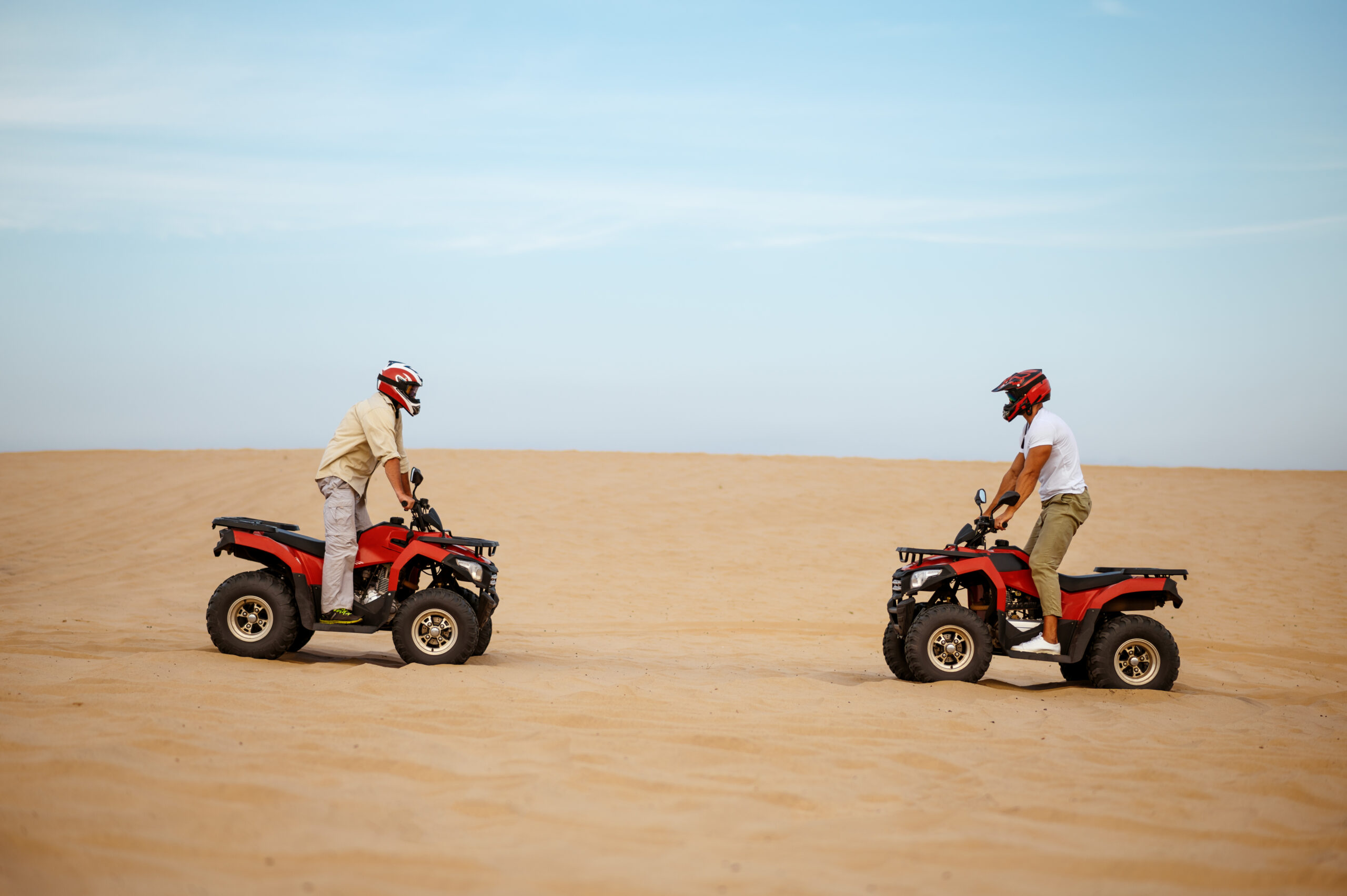 Two racers in helmets stand face to face on atvs, freedom riding in desert. Male persons on quad bikes, sandy race, dune safari in hot sunny day, 4x4 extreme adventure, quad-biking